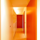 赤い戸と間接照明が白い廊下に奥行きを出す