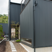 木々の緑に溶け込んだ、黒色ガルバニウムの外壁