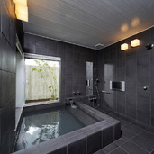 黒のタイル張りが重厚感のある、温泉が引かれた浴室