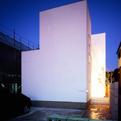 フラットで真っ白な外壁に、サイドから温かみのある光が溢れ出る夜の外観