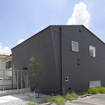 斜めの壁の左官壁、側面はガルバリウム鋼板の大波を採用し、黒い外壁のボリュームに表情を与えた外観