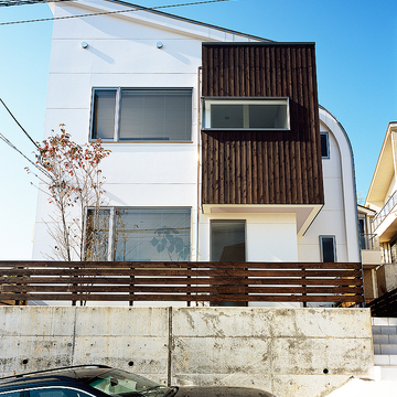 小高い丘に佇む、白と焦げ茶でシンプルな色合いでまとめた立体的な住宅