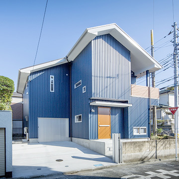 青い空に映えるブルーの外壁にウッド調のドアがアクセントに