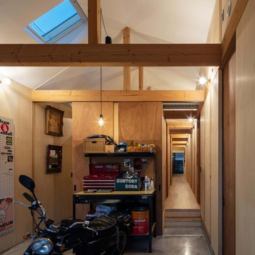 玄関土間夜景。裸電球のブラケットが等間隔に並ぶ架構を照らします。