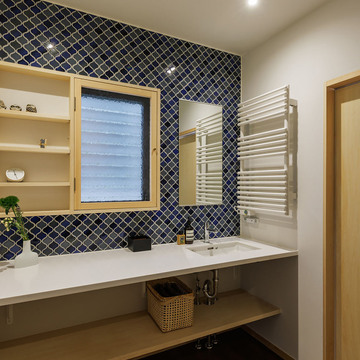 ランタンタイル貼りの洗面室。幅広の人工大理石カウンター。小窓と棚板を組み合わせたキャビネットを既存サッシに嵌め込む。