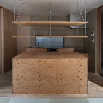 針葉樹合板で造った製作キッチンとアイランドカウンター。キッチン周りの壁面はウレタン塗装したセメント板。両脇に間戸を格納。