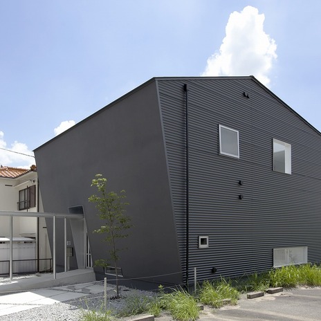 斜めの壁の左官壁、側面はガルバリウム鋼板の大波を採用し、黒い外壁のボリュームに表情を与えた外観