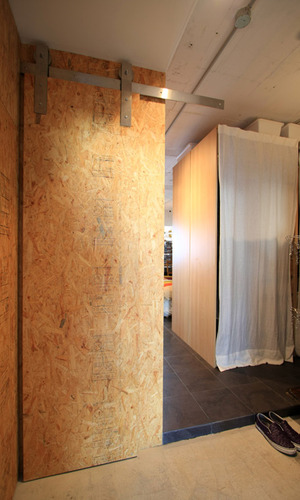 壁の木の荒い仕上げに黒いタイルが映える玄関