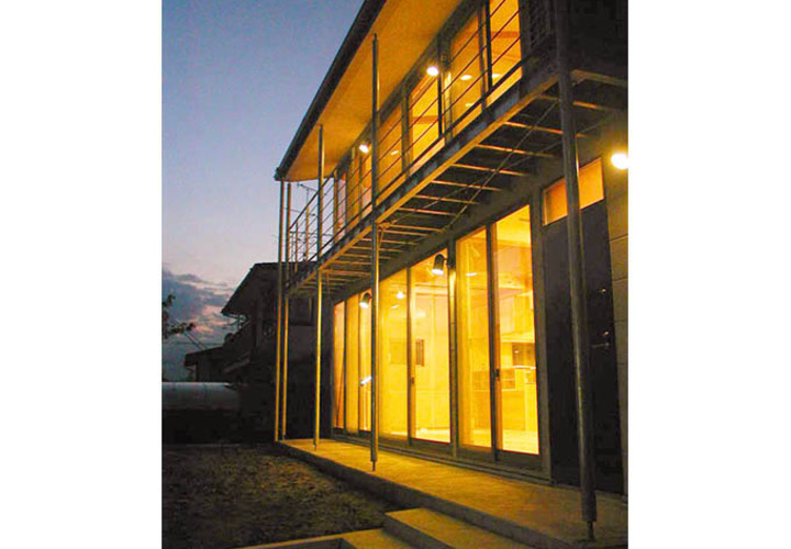 室内の灯りが全面窓から溢れる夕景外観