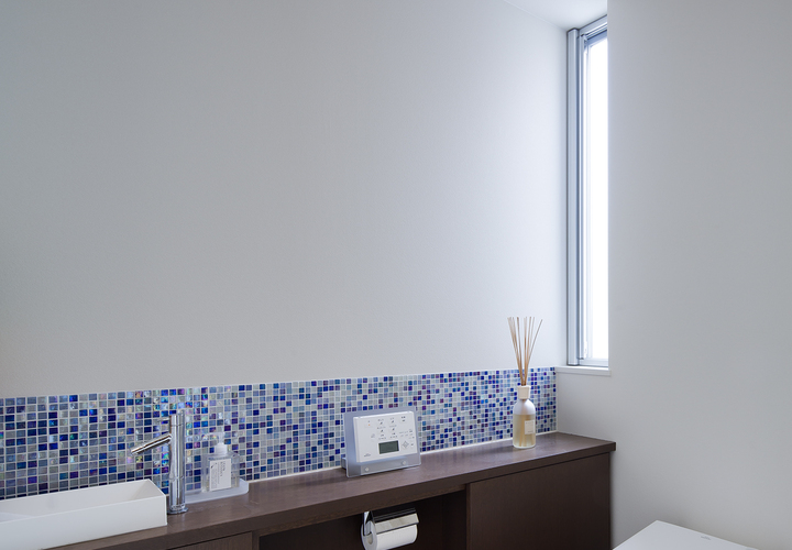 ランダムな水色のタイルが自然光で美しく反射する、広々としたトイレ