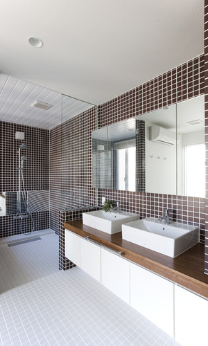 浴室との仕切りガラスが空間に狭さを感じさせない、茶色のタイルが印象的な洗面所