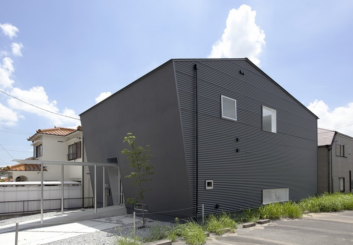斜めの壁の左官壁、側面はガルバリウム鋼板の大波を採用し、黒い外壁のボリュームに表情を与えた外観