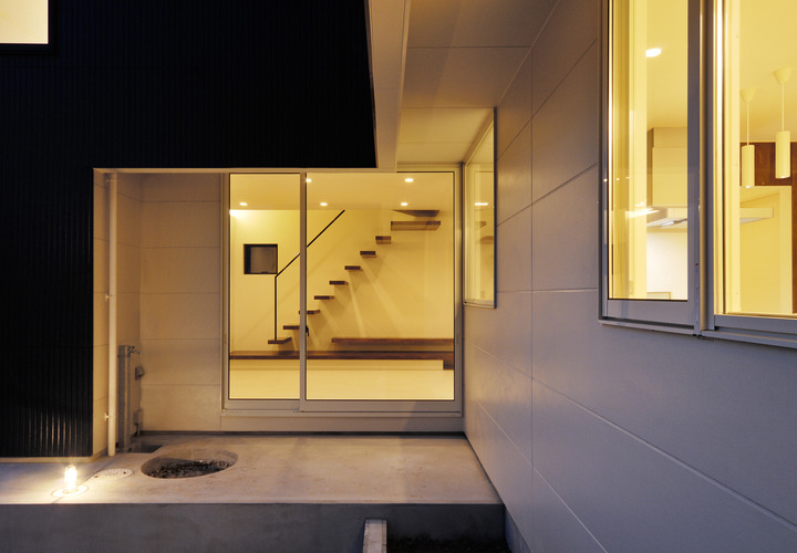 窓から見える室内には、暖かい光の中に彫刻のように美しい階段が見える