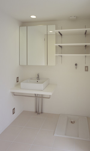 バスルームと同じ白い床タイルを使用した、コンパクトにまとめた洗面所