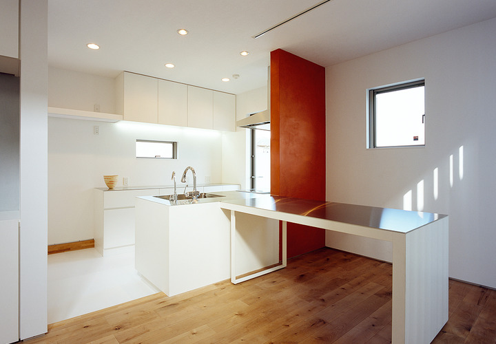 換気扇を背後に設置した赤い壁と、キッチンからＴ字型に伸びるダイニングテーブルが魅力的なダイニングキッチン