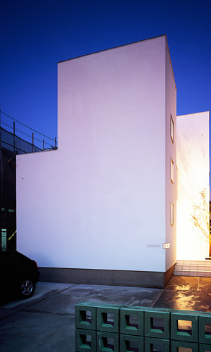 フラットで真っ白な外壁に、サイドから温かみのある光が溢れ出る夜の外観