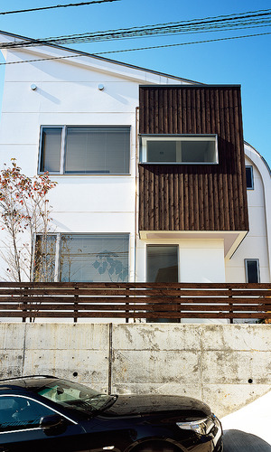 小高い丘に佇む、白と焦げ茶でシンプルな色合いでまとめた立体的な住宅