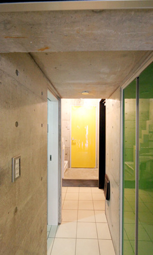 駐車場からエントランスを見る。RC打ち放しと扉のカラーが目を引く