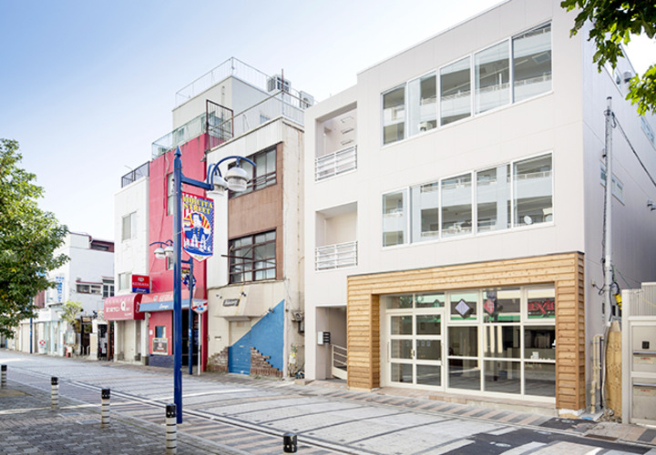 モダンな街並に淡い色の外壁が映える外観