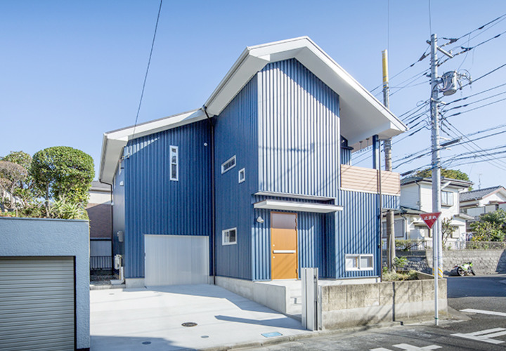 青い空に映えるブルーの外壁にウッド調のドアがアクセントに