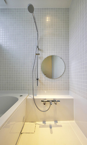 淡いグレーのタイルに円形の鏡がキュートなバスルーム