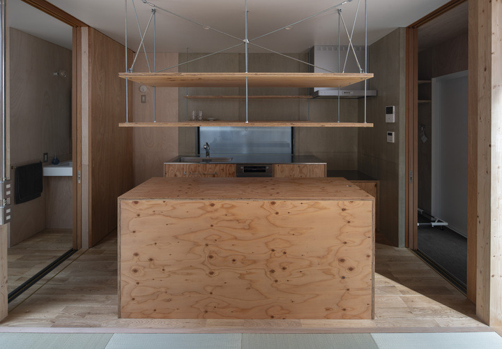 針葉樹合板で造った製作キッチンとアイランドカウンター。キッチン周りの壁面はウレタン塗装したセメント板。両脇に間戸を格納。