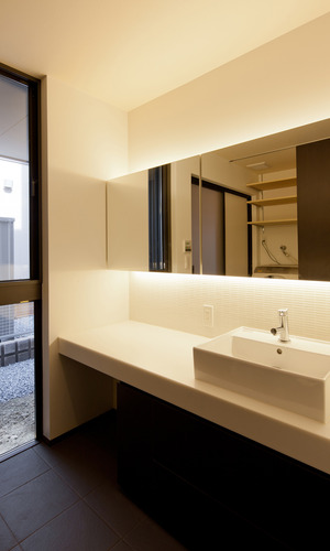 間接照明の柔らかい光と焦げ茶色のタイルが、落ち着いた雰囲気のある洗面空間に