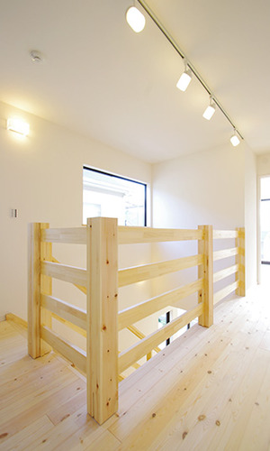 ２階、木製の手すり。無垢材の床と階段を照らす優しい照明。