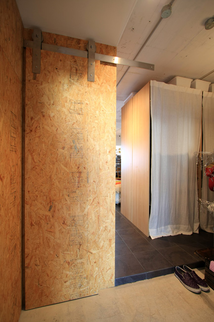 壁の木の荒い仕上げに黒いタイルが映える玄関