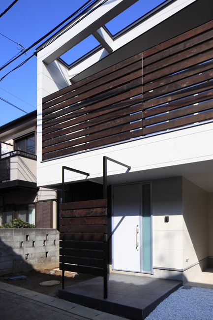 白くシンプルな外壁に木製格子が映えるアプローチ