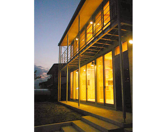 室内の灯りが全面窓から溢れる夕景外観