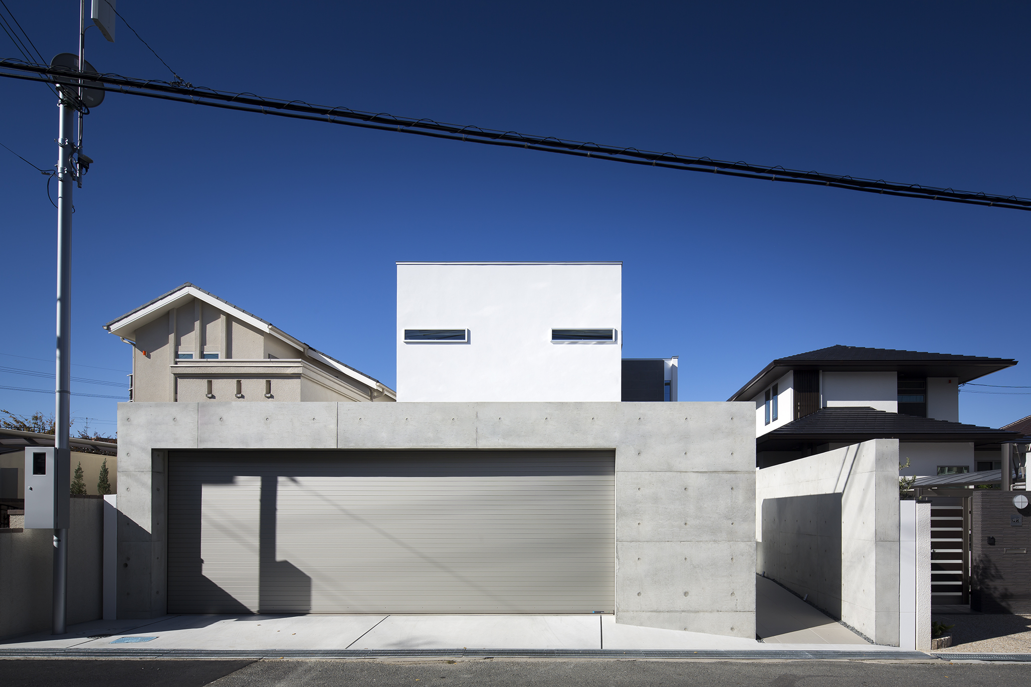 コンクリート打ちっ放し塀とワイドなシャッターが印象的な外観