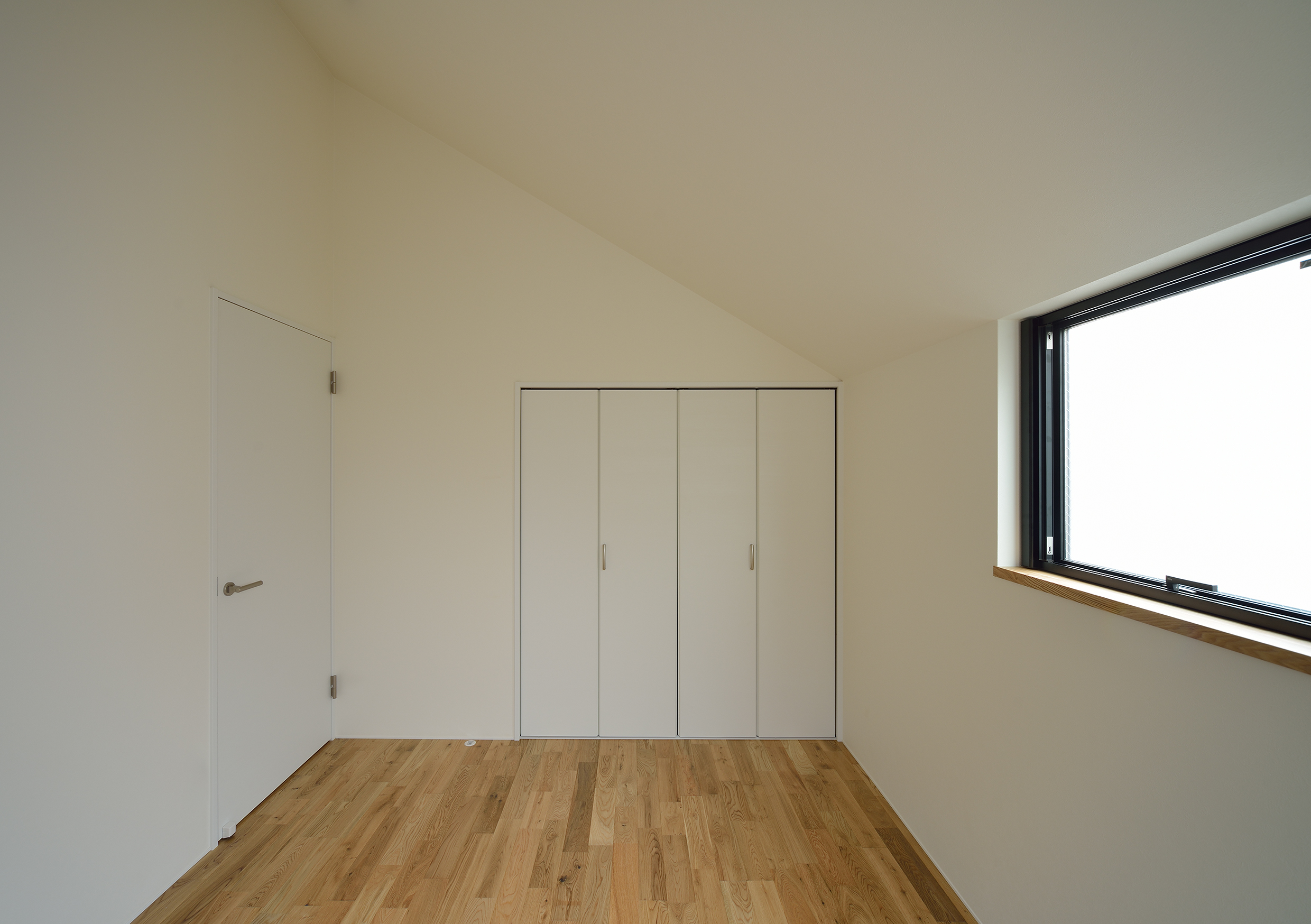 急勾配の屋根面と窓、収納扉の配置が美しい寝室