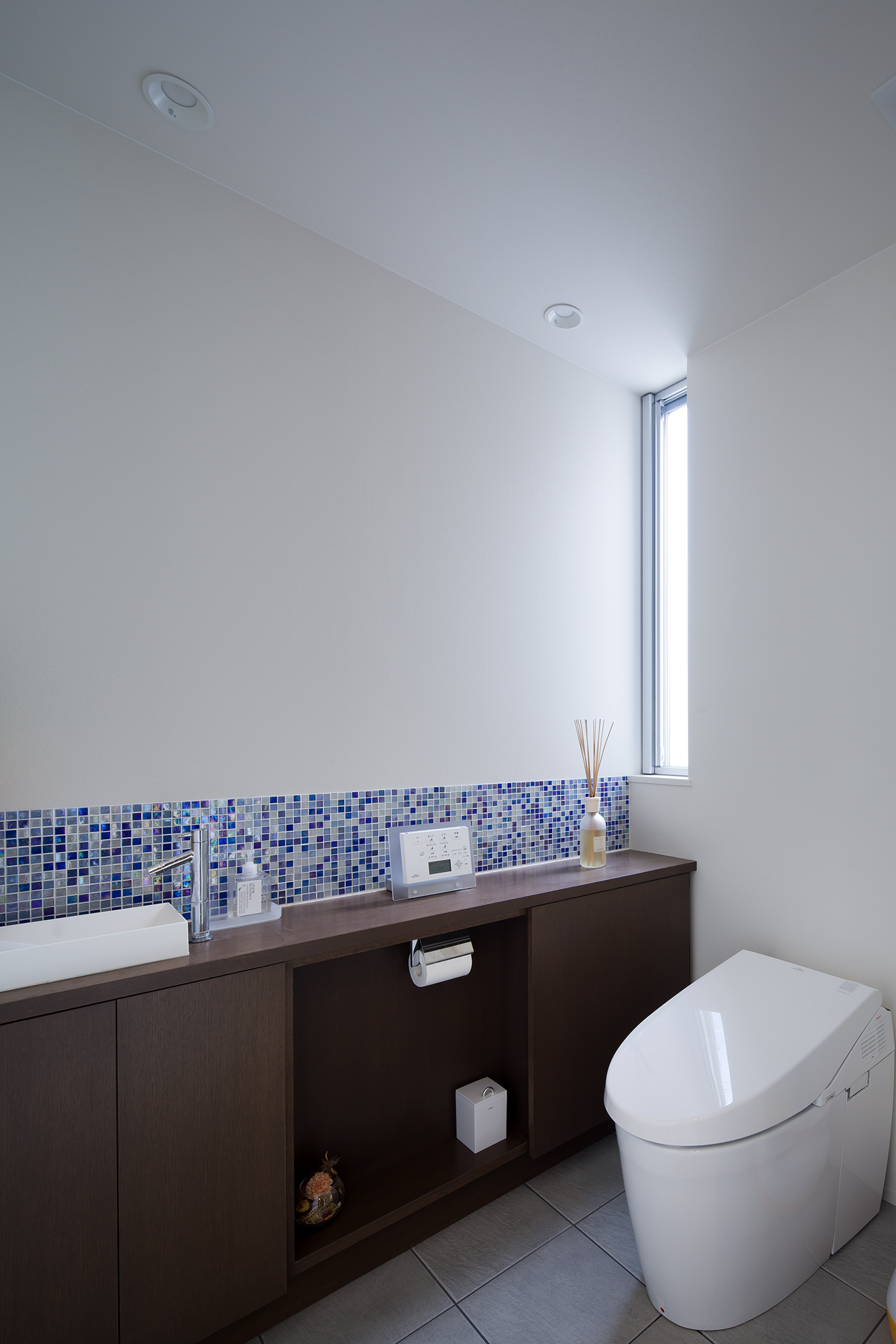 ランダムな水色のタイルが自然光で美しく反射する、広々としたトイレ