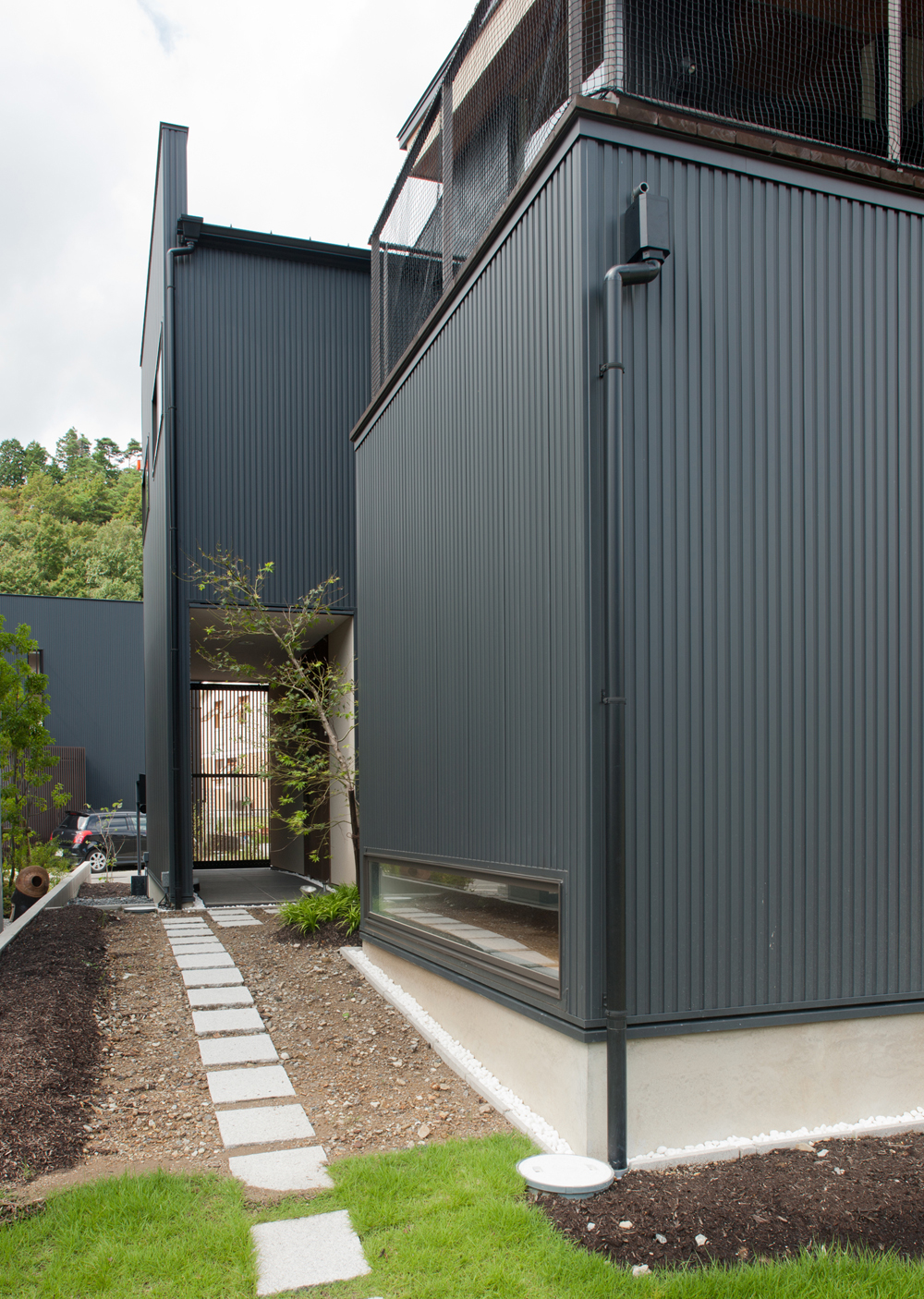 木々の緑に溶け込んだ、黒色ガルバニウムの外壁