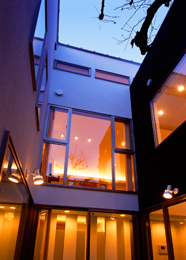 中庭から夜の灯りがもれる家を眺める