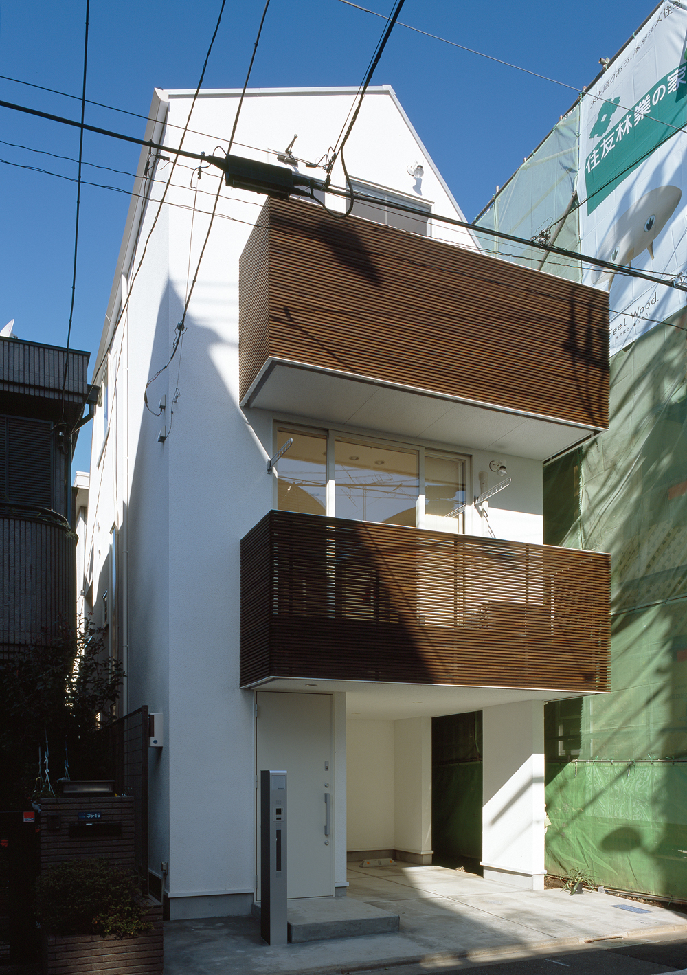 白い外壁と、木目が美しいルーバーが特徴の都市型住宅の外観