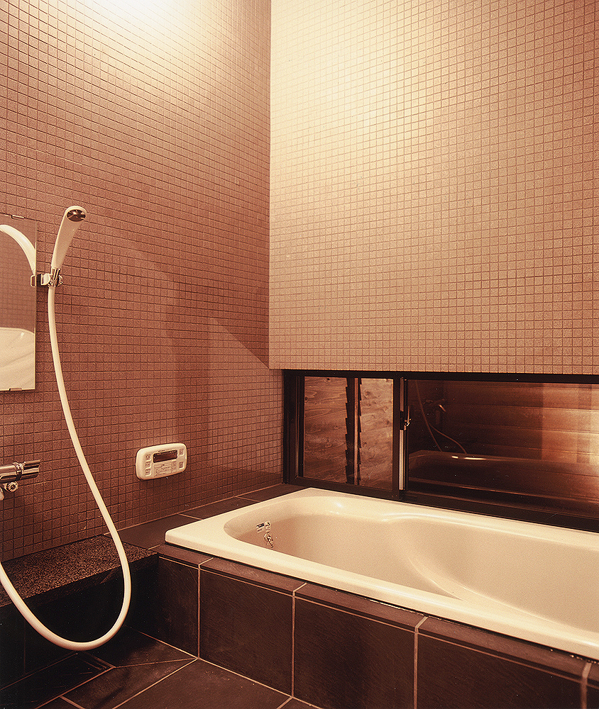 壁面に細かなマットタイル、床面にテクスチャーのある大きめのタイルを使用した、落ち着いた浴室