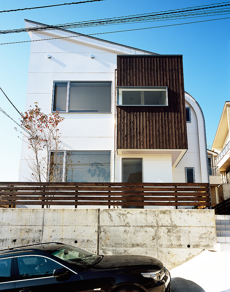 小高い丘に佇む、白と焦げ茶でシンプルな色合いでまとめた立体的な住宅