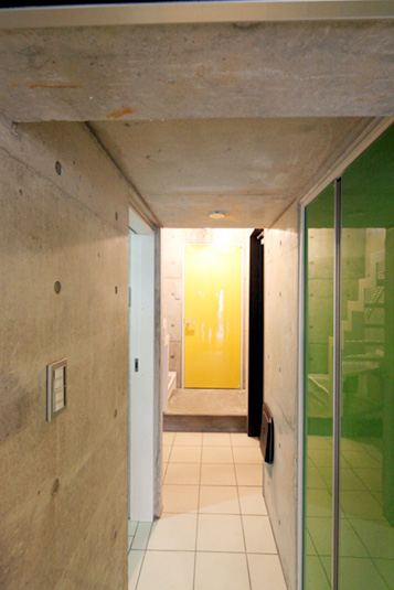 駐車場からエントランスを見る。RC打ち放しと扉のカラーが目を引く