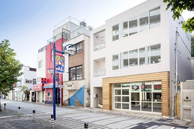 モダンな街並に淡い色の外壁が映える外観