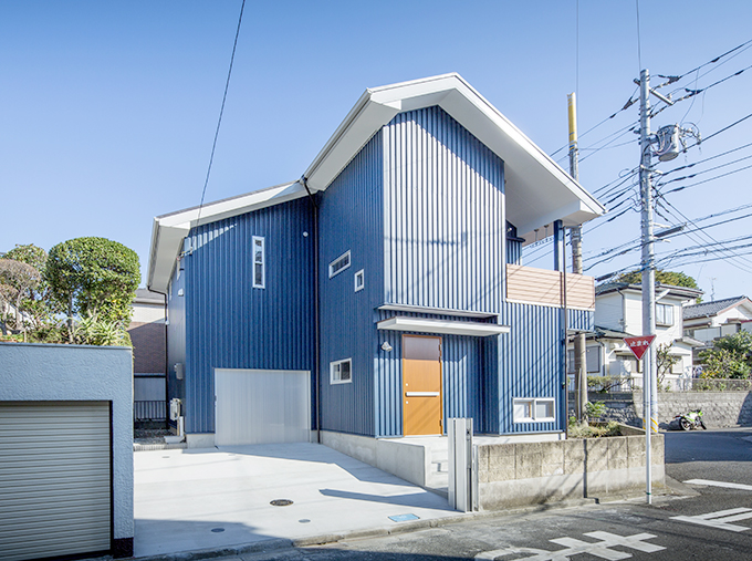 青い空に映えるブルーの外壁にウッド調のドアがアクセントに