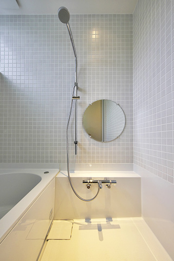 淡いグレーのタイルに円形の鏡がキュートなバスルーム