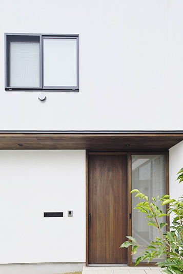 白い壁とコントラストを奏でるウッド調の玄関ドア Fevecasa フェブカーサ