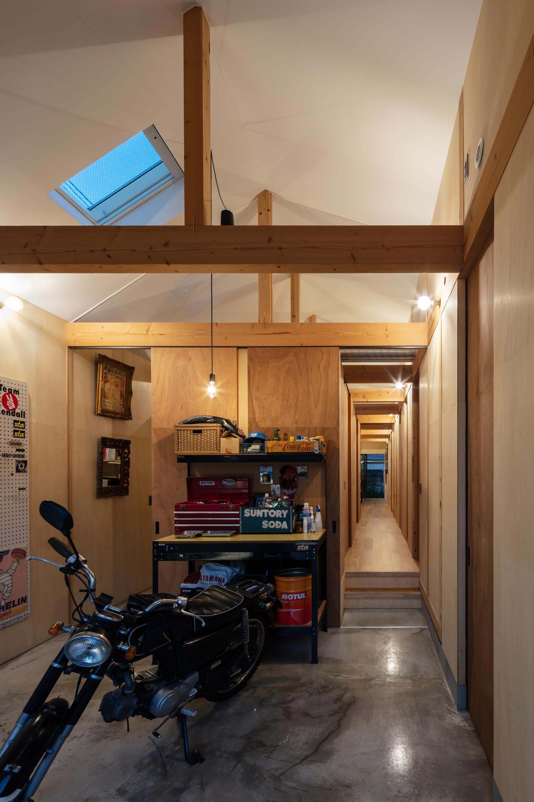 玄関土間夜景。裸電球のブラケットが等間隔に並ぶ架構を照らします。