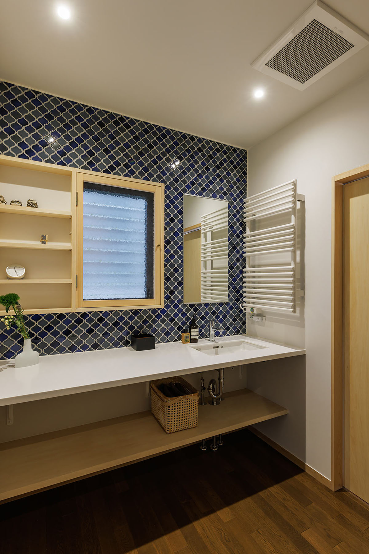 ランタンタイル貼りの洗面室。幅広の人工大理石カウンター。小窓と棚板を組み合わせたキャビネットを既存サッシに嵌め込む。