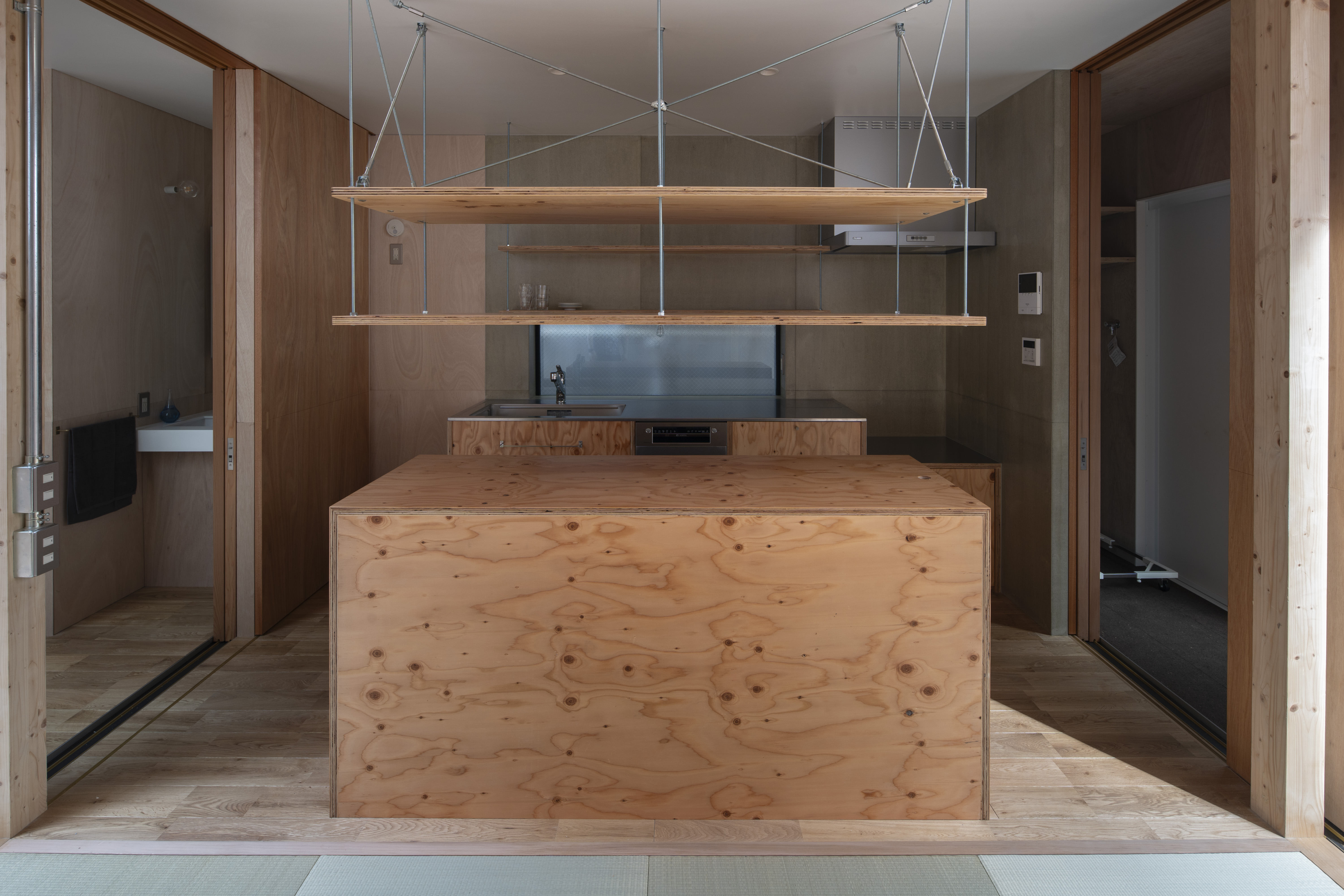 針葉樹合板で造った製作キッチンとアイランドカウンター。キッチン周りの壁面はウレタン塗装したセメント板。両脇に間戸を格納。